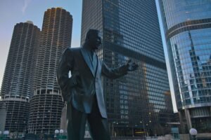 Photograph of Irv Kupcinet statue against Chicago's iconic skyscrapers during the day.