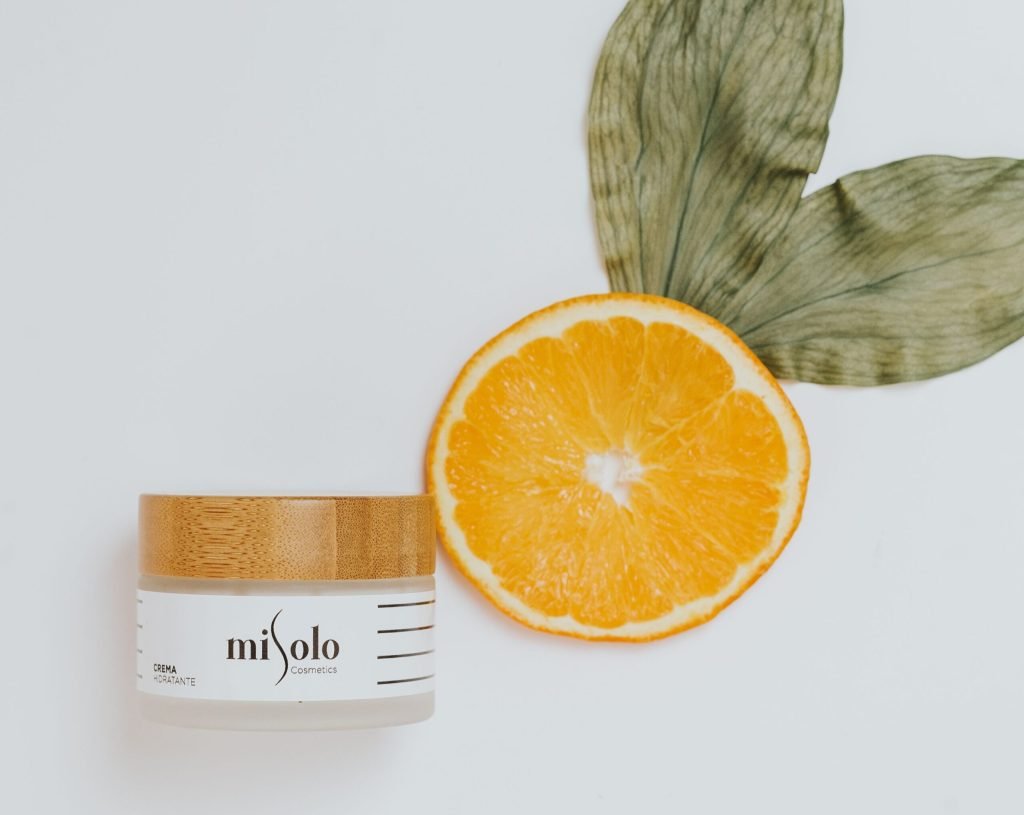 Overhead view of skincare cream with natural ingredients like orange and leaves for luxurious beauty.